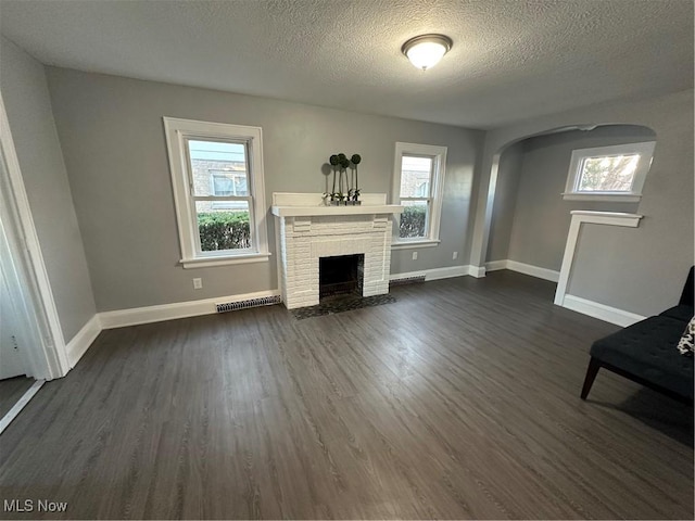 unfurnished living room with dark wood-type flooring, a healthy amount of sunlight, and a brick fireplace