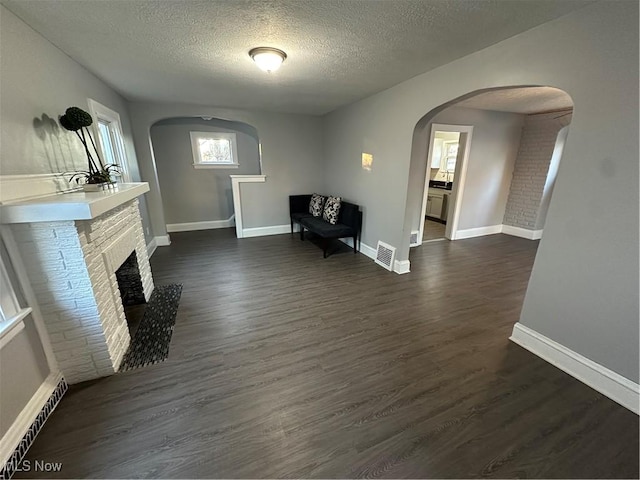 unfurnished room featuring dark hardwood / wood-style flooring, a textured ceiling, and a brick fireplace