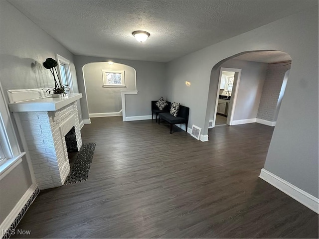 unfurnished room with a textured ceiling, dark hardwood / wood-style floors, and a brick fireplace