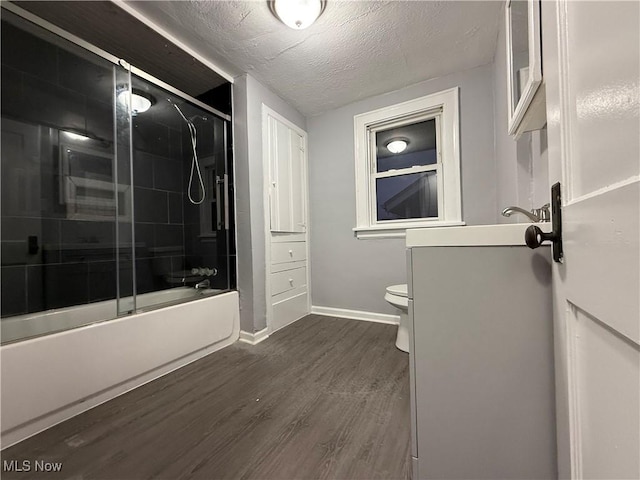 bathroom with hardwood / wood-style flooring, toilet, shower / bath combination with glass door, and a textured ceiling