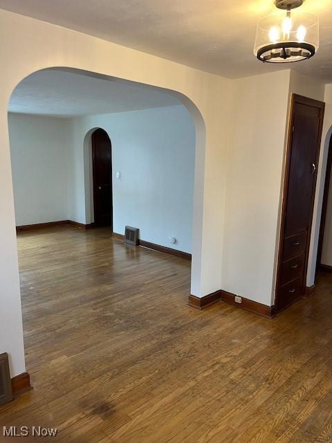 spare room with a notable chandelier and dark hardwood / wood-style flooring