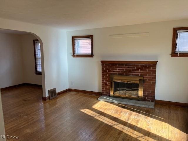 unfurnished living room with dark wood-type flooring, a healthy amount of sunlight, and a brick fireplace