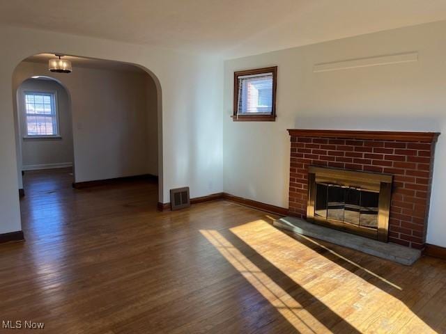 unfurnished living room with dark wood-type flooring, a wealth of natural light, and a brick fireplace