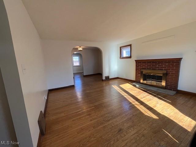 unfurnished living room with dark hardwood / wood-style flooring and a brick fireplace