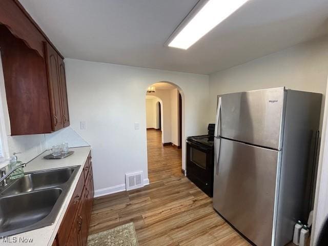 kitchen with stainless steel refrigerator, sink, light wood-type flooring, and black range with electric cooktop