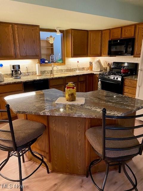 kitchen with stone counters, tasteful backsplash, light hardwood / wood-style flooring, a breakfast bar, and black appliances