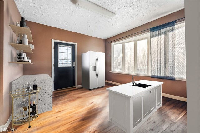 interior space featuring stainless steel refrigerator with ice dispenser, light wood-type flooring, a textured ceiling, sink, and white cabinets