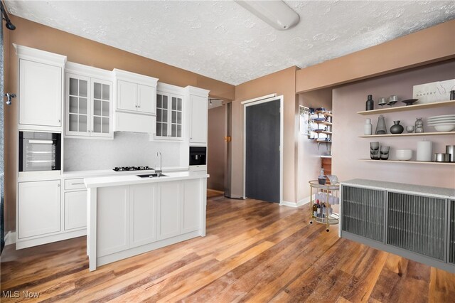 kitchen featuring oven, a textured ceiling, a kitchen island with sink, white cabinets, and light wood-type flooring