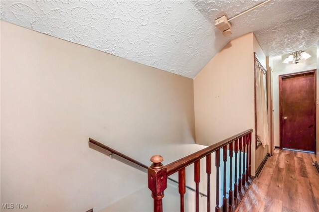 stairs with hardwood / wood-style floors, lofted ceiling, and a textured ceiling