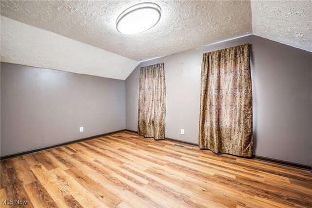 additional living space featuring a textured ceiling, vaulted ceiling, and light hardwood / wood-style flooring