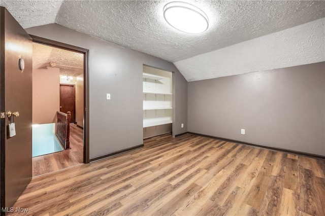 additional living space with a textured ceiling, light hardwood / wood-style floors, and lofted ceiling