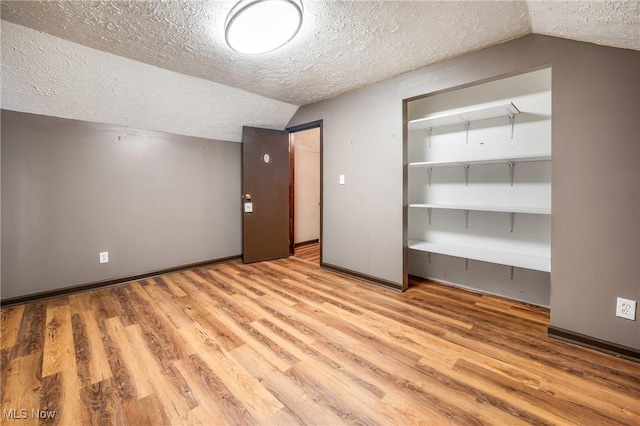 unfurnished bedroom with a textured ceiling, light hardwood / wood-style floors, a closet, and lofted ceiling