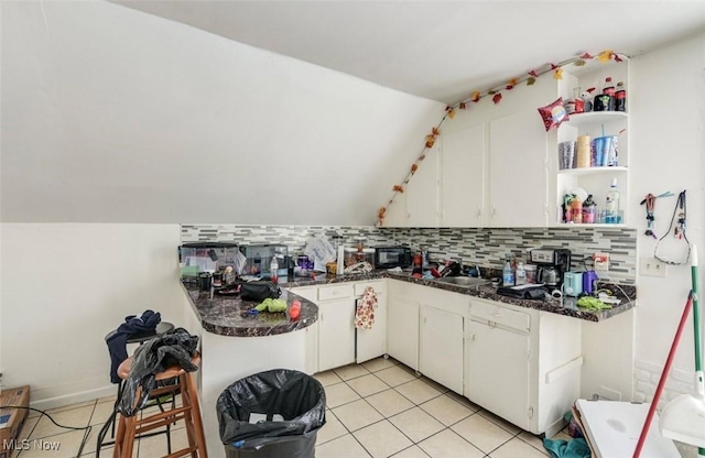 kitchen with backsplash, vaulted ceiling, sink, light tile patterned floors, and white cabinets