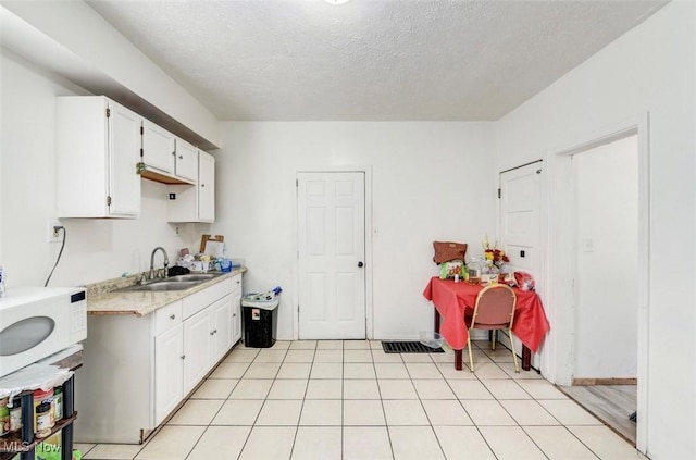 kitchen with sink, white cabinets, a textured ceiling, and light wood-type flooring