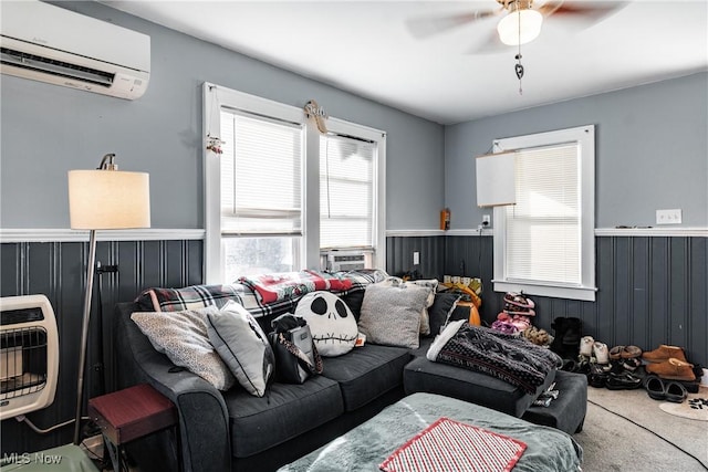 carpeted living room with a wall mounted air conditioner, heating unit, cooling unit, ceiling fan, and wooden walls