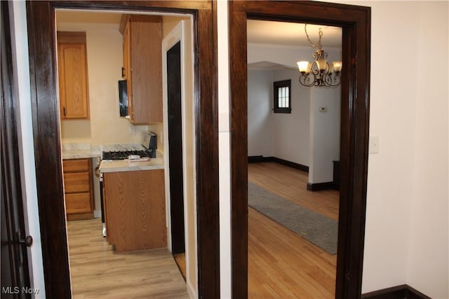 corridor with crown molding, a chandelier, and light wood-type flooring