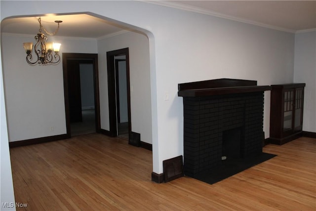 unfurnished living room featuring a notable chandelier, wood-type flooring, ornamental molding, and a brick fireplace