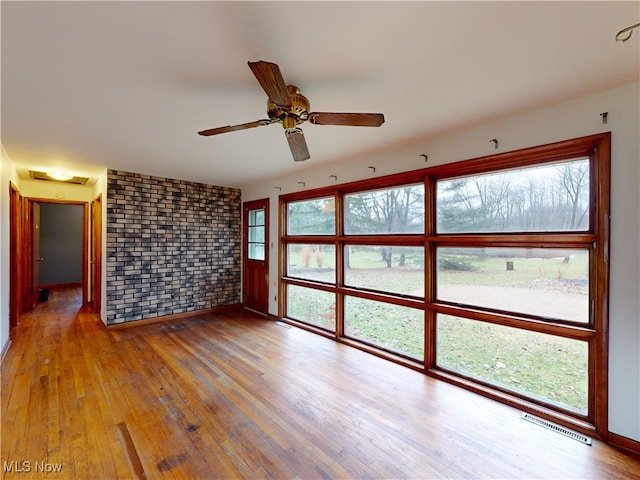 unfurnished room with hardwood / wood-style flooring, ceiling fan, and brick wall