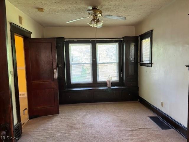 unfurnished room with a textured ceiling, ceiling fan, and light carpet