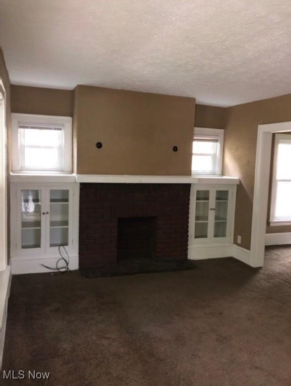 unfurnished living room with dark colored carpet, a textured ceiling, and a brick fireplace