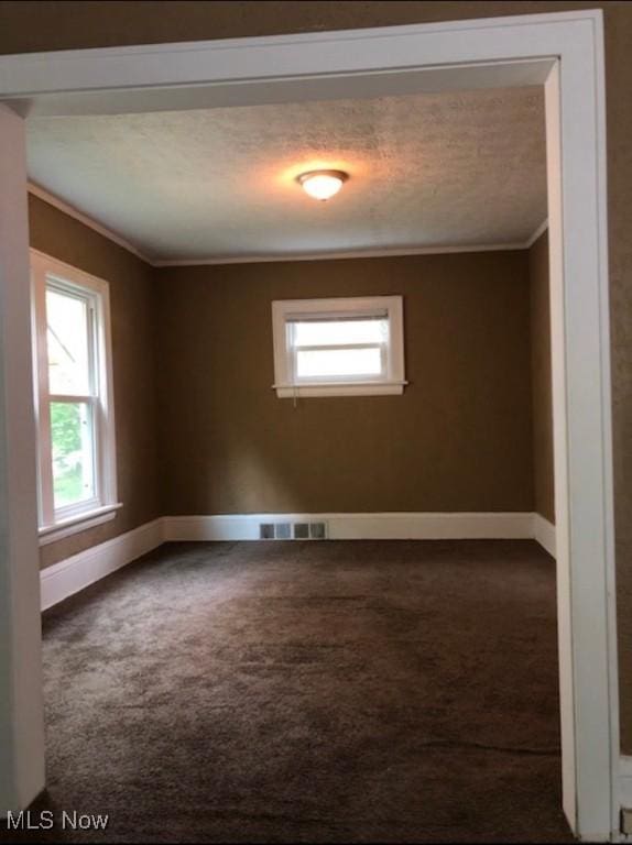 spare room with a textured ceiling, dark carpet, and crown molding