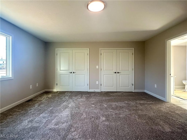 unfurnished bedroom with connected bathroom, carpet floors, and multiple closets