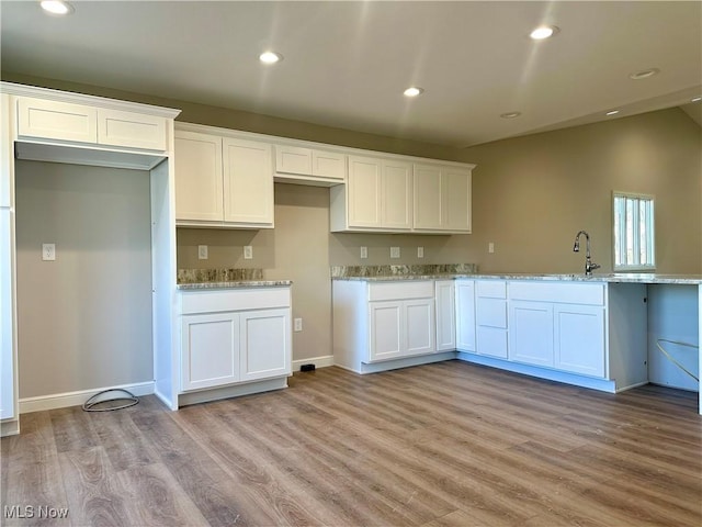 kitchen with white cabinets, light stone counters, light wood-type flooring, and sink