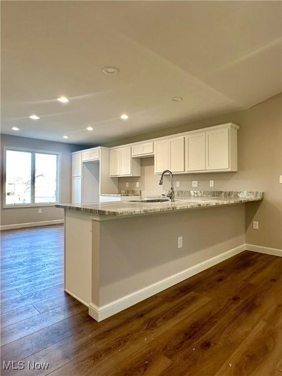 kitchen with sink, dark wood-type flooring, light stone counters, kitchen peninsula, and white cabinets