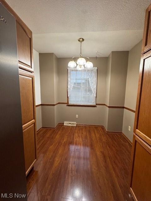 unfurnished dining area with a chandelier, a textured ceiling, and dark wood-type flooring