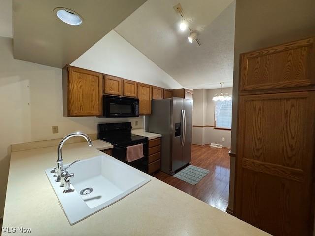 kitchen featuring sink, dark hardwood / wood-style floors, vaulted ceiling, decorative light fixtures, and black appliances