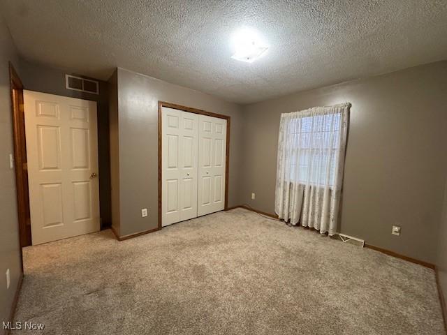 unfurnished bedroom featuring a textured ceiling, light colored carpet, and a closet