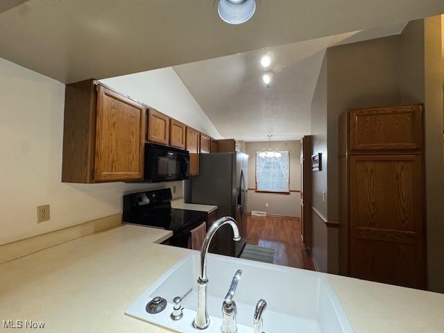 kitchen featuring vaulted ceiling, sink, black appliances, hardwood / wood-style flooring, and a chandelier