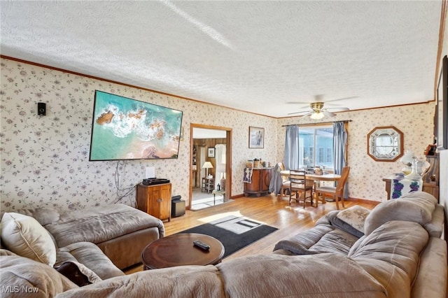 living room with ceiling fan, crown molding, a textured ceiling, and light wood-type flooring