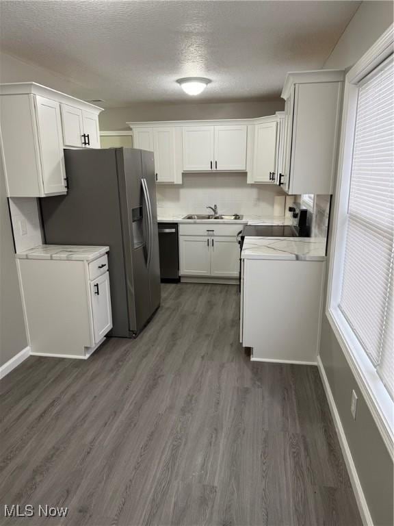 kitchen with sink, dark wood-type flooring, stainless steel appliances, light stone counters, and white cabinets