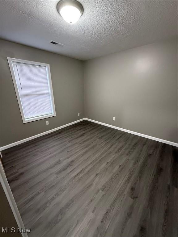 empty room featuring a textured ceiling and dark hardwood / wood-style floors