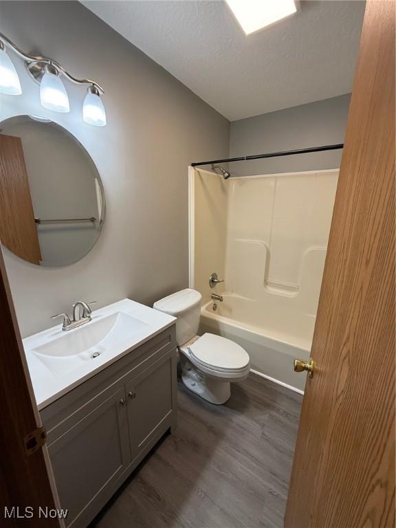 full bathroom featuring vanity, a textured ceiling, shower / tub combination, hardwood / wood-style flooring, and toilet