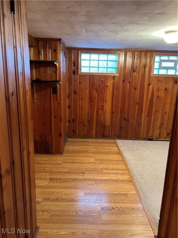 basement featuring a wealth of natural light, wood walls, a textured ceiling, and light hardwood / wood-style flooring