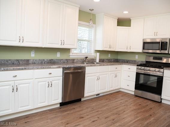 kitchen with white cabinets, appliances with stainless steel finishes, dark hardwood / wood-style floors, and pendant lighting