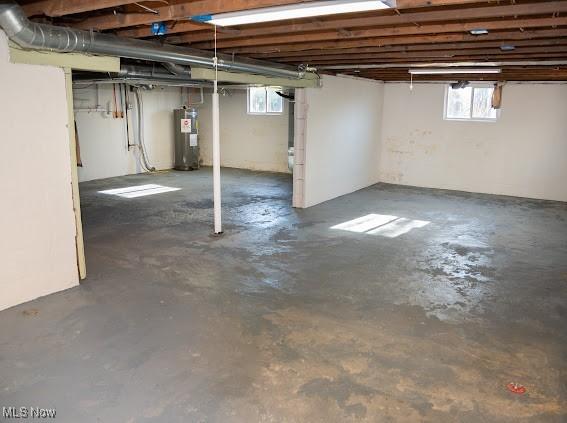 basement with electric water heater and a healthy amount of sunlight