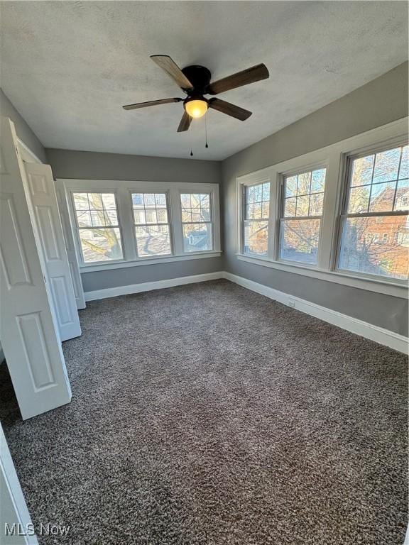 interior space featuring multiple windows, ceiling fan, dark carpet, and a textured ceiling