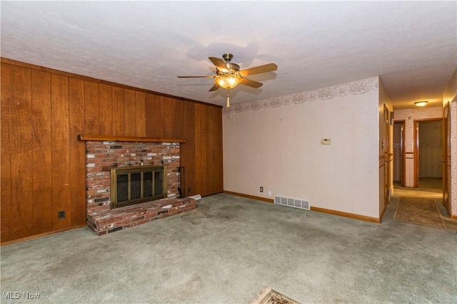 unfurnished living room featuring light carpet, a textured ceiling, ceiling fan, a fireplace, and wood walls