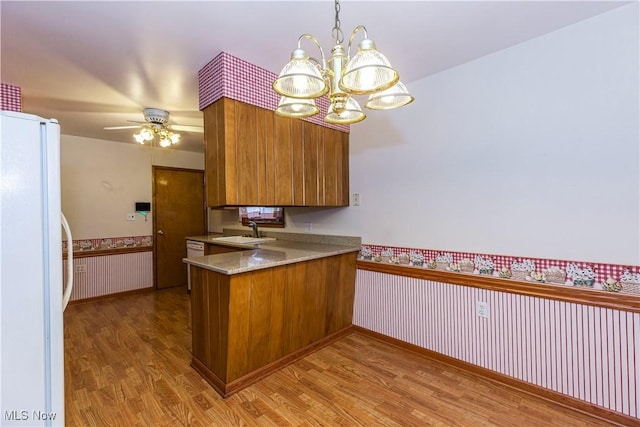 kitchen featuring kitchen peninsula, white appliances, ceiling fan with notable chandelier, sink, and hardwood / wood-style flooring