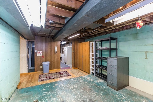 basement with hardwood / wood-style floors, white fridge, and wooden walls