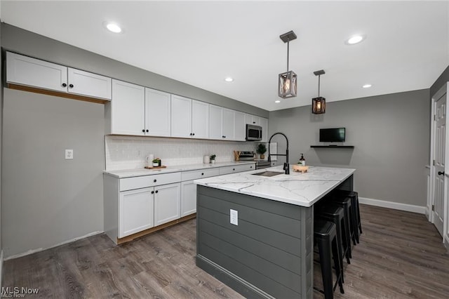 kitchen with light stone countertops, sink, white cabinets, hanging light fixtures, and an island with sink