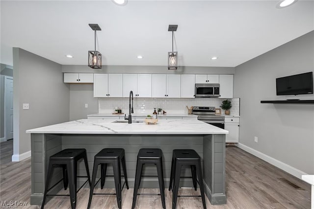 kitchen featuring a large island with sink, light stone counters, light hardwood / wood-style floors, and appliances with stainless steel finishes