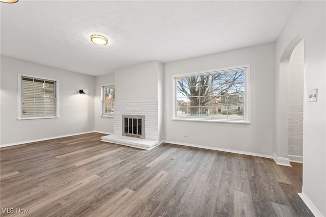 unfurnished living room featuring dark wood-type flooring and a brick fireplace