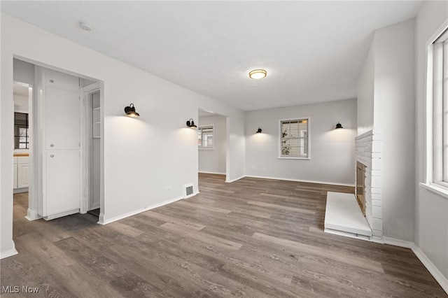 unfurnished living room featuring a stone fireplace, plenty of natural light, and dark hardwood / wood-style floors