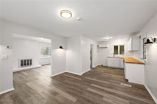 kitchen with wooden counters, sink, white cabinets, dark hardwood / wood-style floors, and a stone fireplace