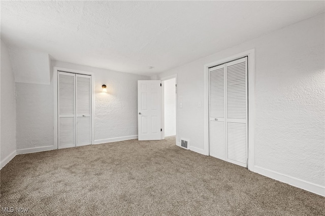 unfurnished bedroom with carpet flooring, a textured ceiling, and two closets