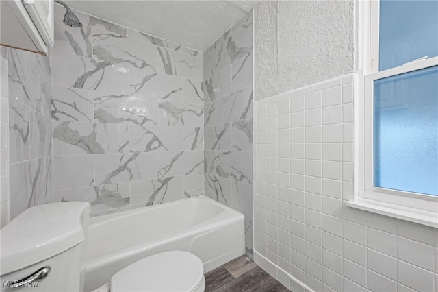 bathroom featuring toilet, tiled shower / bath, tile walls, and hardwood / wood-style flooring